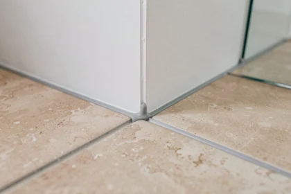 Joint de dilatation discret en silicone gris clair entre carrelage grand format et mur de salle de bain moderne